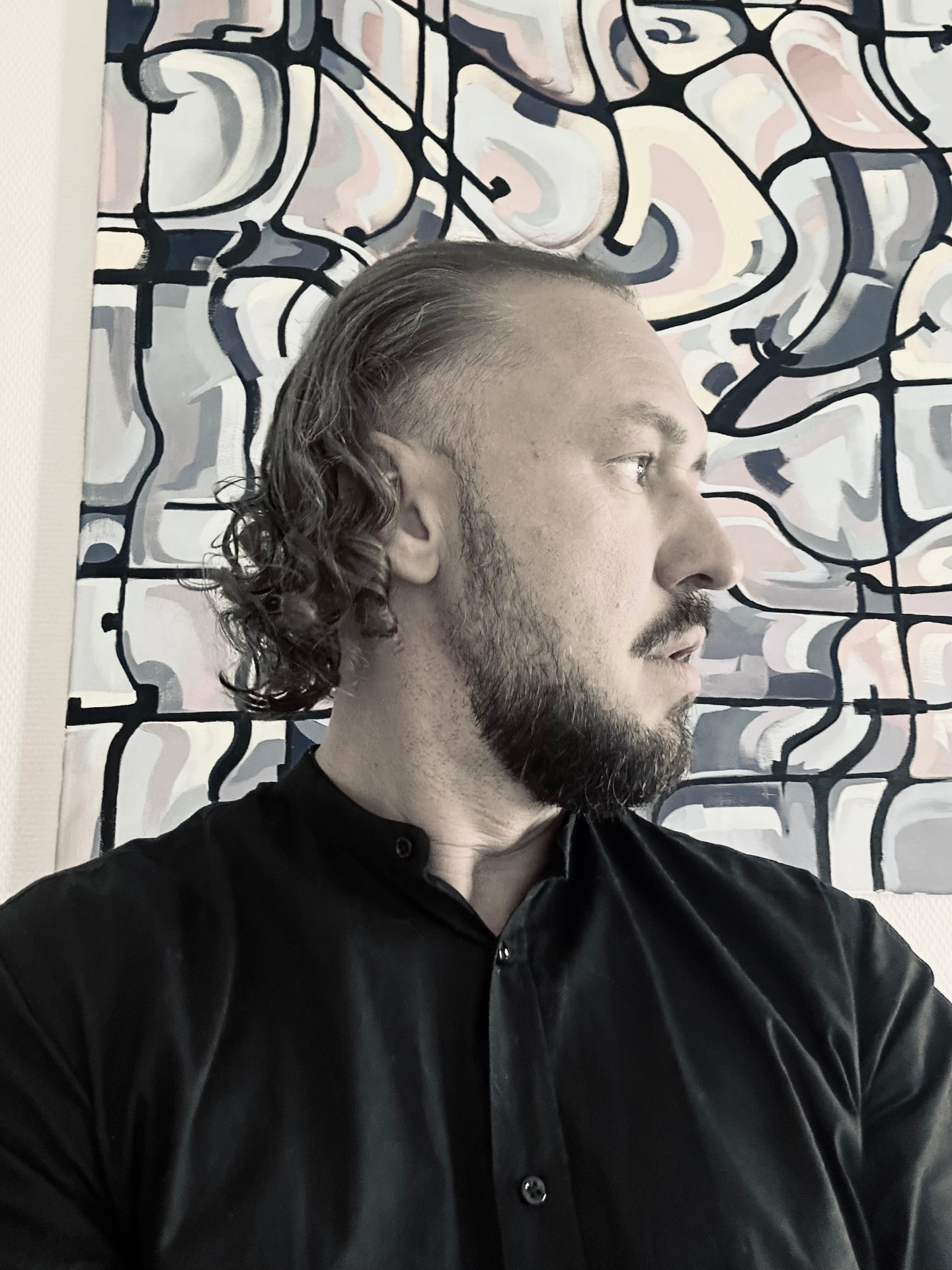 Composer and pianist Vlad Krik in profile before a painting of colour fields divided by dark frames